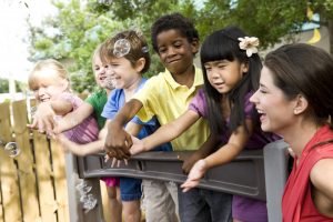 5 preschool children playing on playground with teacher