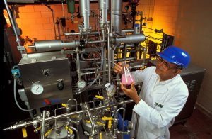 A photo of a man working in a factory examining a liquid product in a beaker