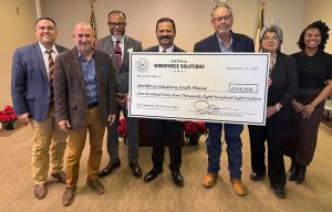 Group of professionals standing indoors holding a large Texas Workforce Solutions grant check.